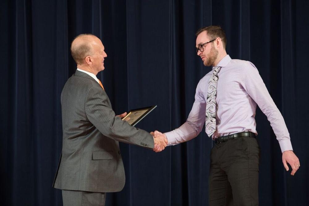 Doctor Potteiger shaking hands with an award recipient with a light lavender shirt and swirl pattern tie